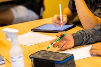 Ein Schüler hält beim Unterricht in seiner Klasse einen Stift, während ein anderer mit einem Tablet arbeitet.