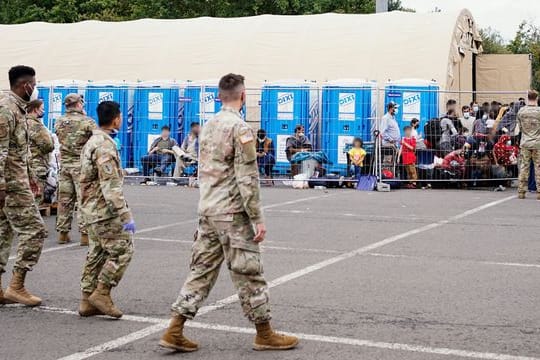 Aus Afghanistan evakuierte Menschen stehen auf der Ramstein Air Base vor einem Zelt.