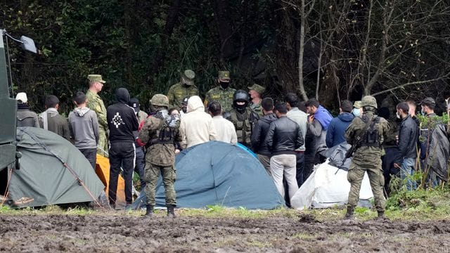 Migranten, die an der Grenze zu Belarus festsitzen, werden von polnischen Beamten umstellt. Migranten, die an der Grenze zu Belarus festsitzen, werden von polnischen Beamten umstellt.