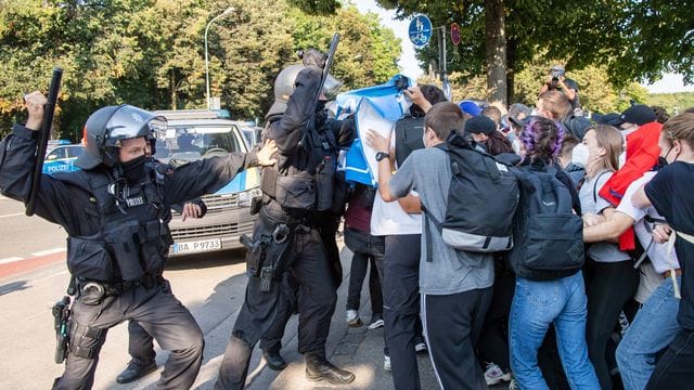 Ein Polizist hebt vor einer Gruppe von Demonstranten seinen Schlagstock.