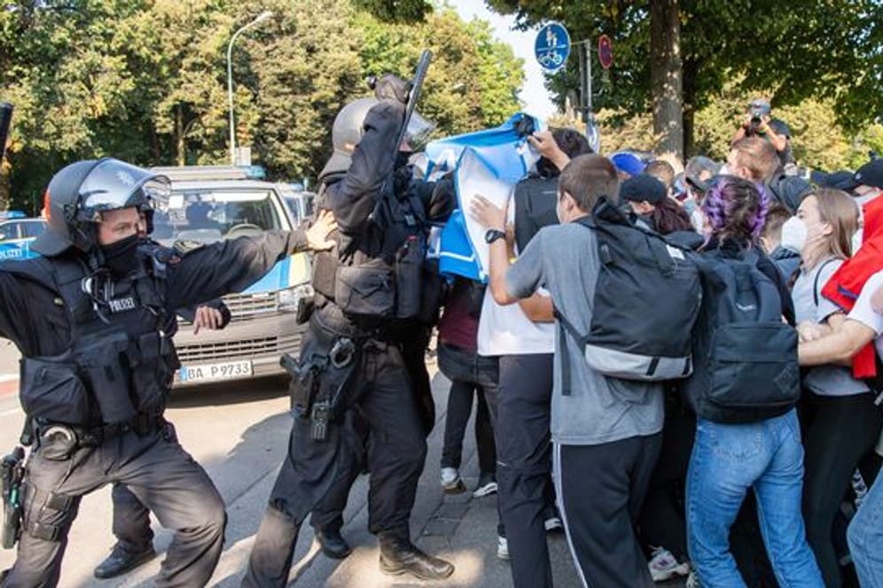 Ein Polizist hebt vor einer Gruppe von Demonstranten seinen Schlagstock.