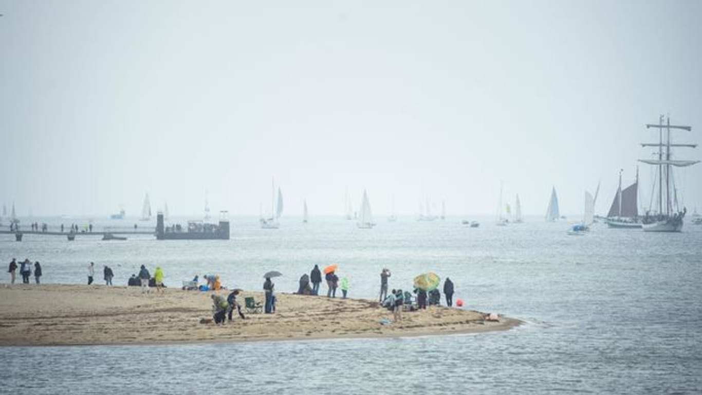 Menschen beobachten Segelschiffe während der traditionellen Windjammerparade zum Abschluss der Kieler Woche in der Kieler Förde.