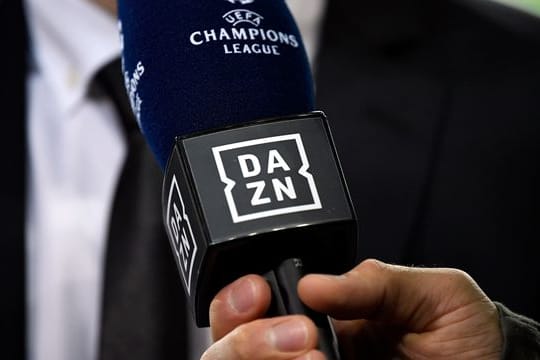 Ein Reporter hält ein Mikrofon des Streamingdienstes DAZN während eines Interviews fest.