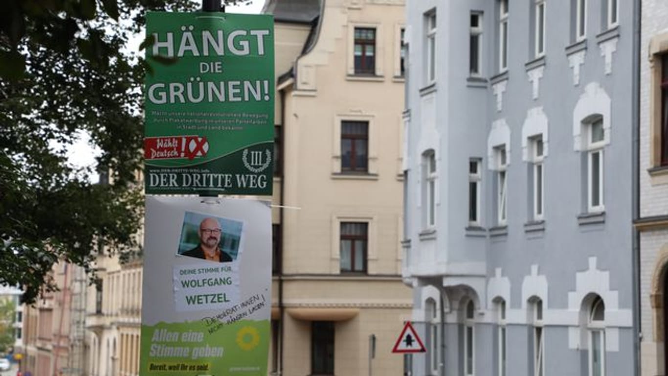 Ein umstrittenes Wahlplakat der Splitterpartei "III Weg" hängt über einem Plakat der Grünen.