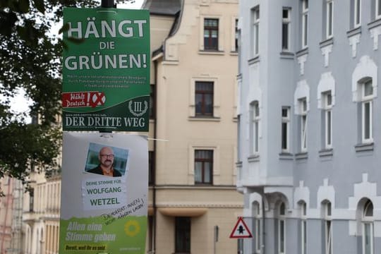 Ein umstrittenes Wahlplakat der Splitterpartei "III Weg" hängt über einem Plakat der Grünen.