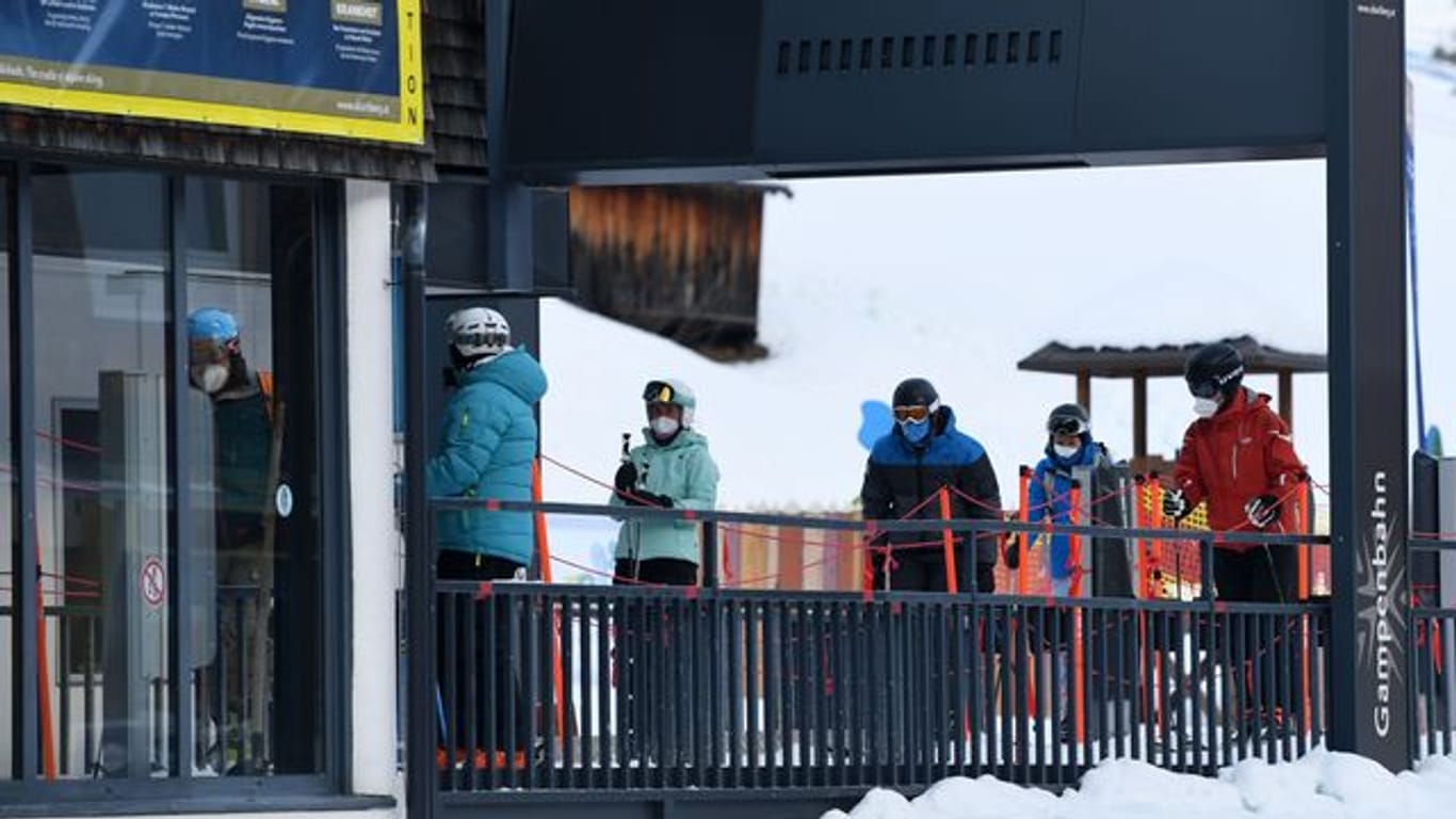 Wintersportler stehen in Tirol mit Mund-Nasen-Schutz an einem Skilift an.
