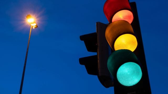 Eine Ampel zeigt am frühen Morgen die Farben rot, gelb und grün.
