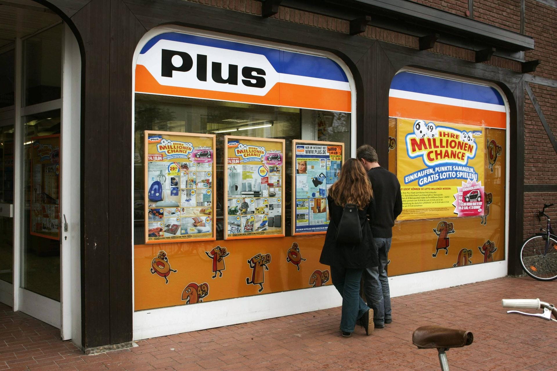 Passanten vor einem Plus-Laden in Cuxhaven im Jahr 2004: Die "Plus Warenhandelsgesellschaft" war eine Discounter-Kette des Tengelmann-Konzerns, die seit 1972 bestand. Anders als die Konkurrenz von Aldi, Lidl oder Norma gab es in den rund 2.900 Plus-Filialen ein größeres Sortiment und mehr Markenartikel. Bis 2010 wurden die Filialen zu Edeka-Geschäften umgeflaggt, einige gingen an Rewe und wurden zu Penny-Märkten.