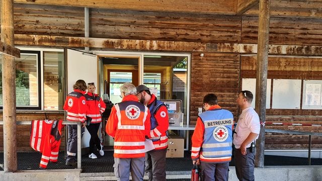 Mitarbeiter des Deutschen Roten Kreuzes stehen vor einer Berghütte: Eine ganze Gruppe musste wegen einer Magen-Darm-Erkrankung ins Tal gebracht werden.