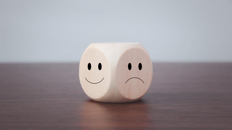 Ein Würfel mit lachendem und traurigem Smiley: Bei einer bipolaren Störung schwankt die Stimmung zwischen Manie und Depression.