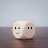 Ein Würfel mit lachendem und traurigem Smiley: Bei einer bipolaren Störung schwankt die Stimmung zwischen Manie und Depression.