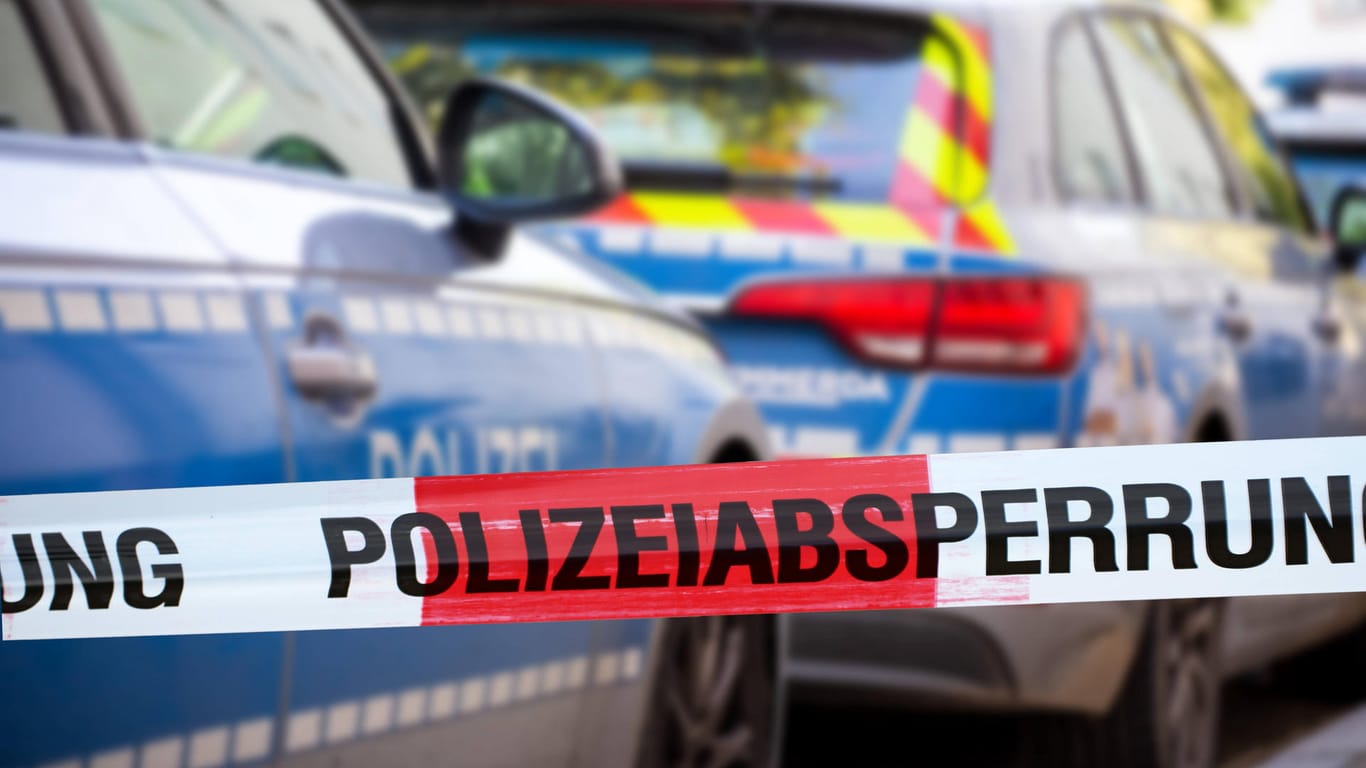 Polizeiabsperrung mit Polizeiauto im Hintergrund (Symbolbild): In München ist ein Mann nach einem Streit in einer Obdachlosenunterkunft tot aufgefunden worden.