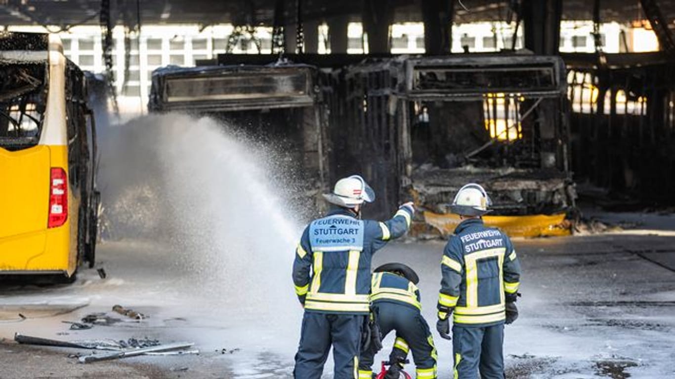 Feuerwehrmänner stehen bei Nachlöscharbeiten vor ausgebrannte Bussen: Noch kann die Halle nicht betreten werden.