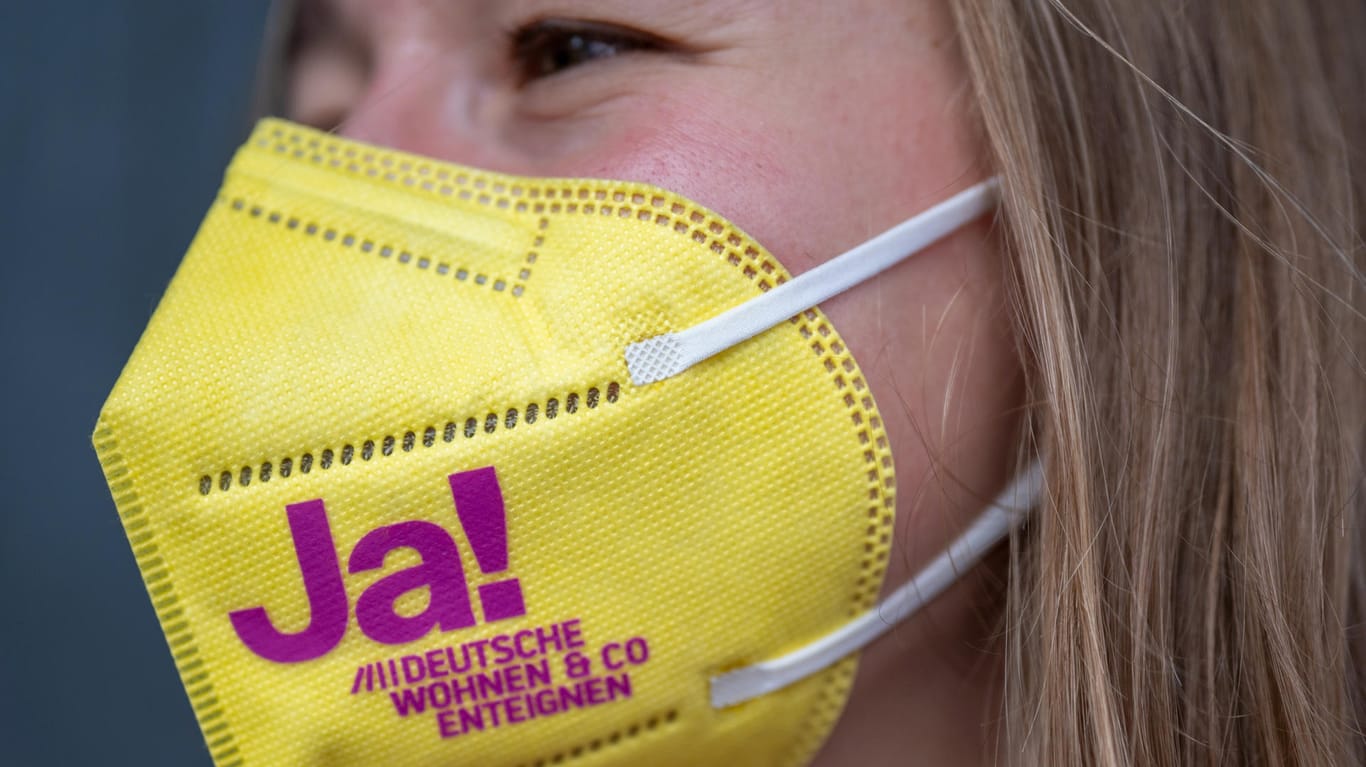 Eine Unterstützerin der Initiative "Deutsche Wohnen & Co. enteignen" trägt eine Maske mit einem deutlichen Bekenntnis zur Enteignung.