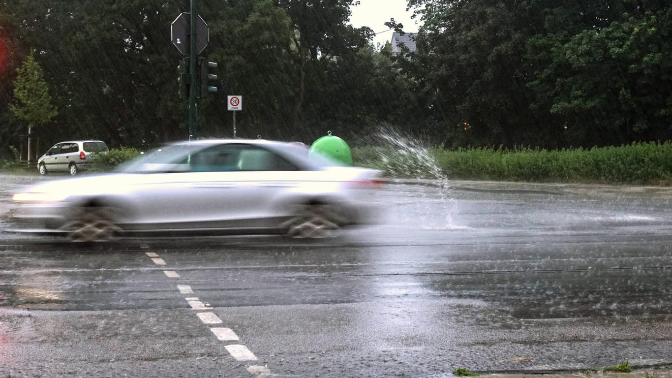 Ein Auto fährt über eine Straße mit Wasser (Archivbild): In NRW werden kräftige Regenschauer und Gewitter erwartet.