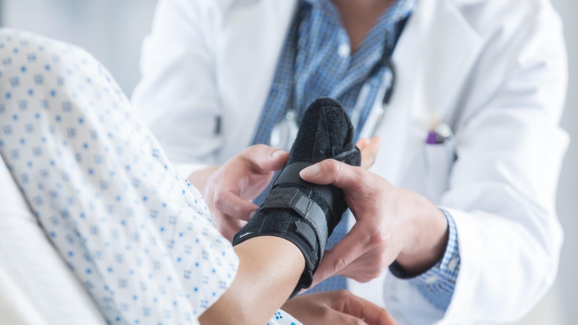 Patientin mit Armmanschette im Gespräch mit einem Arzt. Rheumatisch bedingte Gelenkschmerzen können sehr schmerzhaft sein. Manchmal bringt nur eine Operation Linderung.