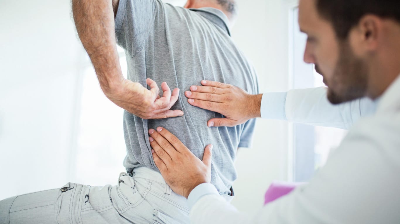 Ein älterer Mann mit Rückenschmerzen beim Arzt. Mit zunehmendem Alter steigt auch bei Männern das Risiko, an Osteoporose zu erkranken.
