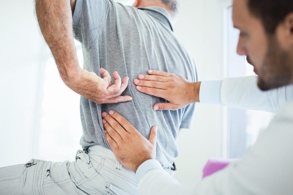 Ein älterer Mann mit Rückenschmerzen beim Arzt. Mit zunehmendem Alter steigt auch bei Männern das Risiko, an Osteoporose zu erkranken.