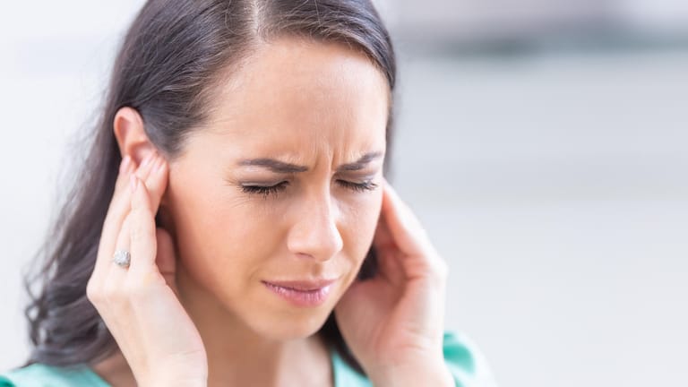 Eine Frau fasst sich an die Ohren. Stress kann das Hörvermögen negativ beeinflussen.