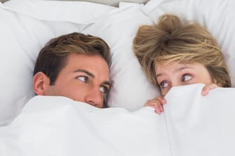 Ein Paar liegt im Bett und schaut sich besorgt an. Bakterielle Infektionen im Intimbereich können durch Geschlechtsverkehr an den Partner weitergegeben werden.