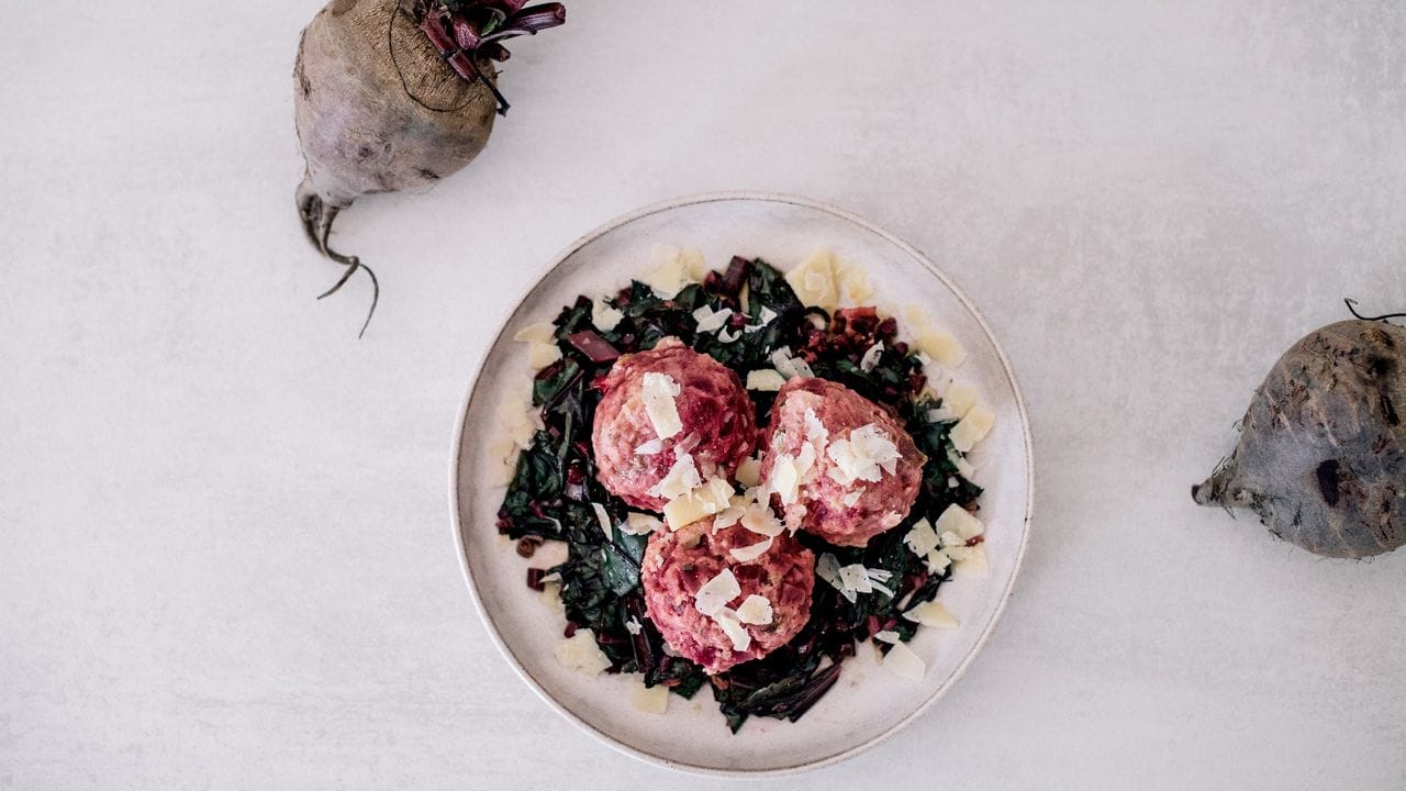 Serviert werden die purpurroten Knödel auf in Butter gedünstete Blätter und Stiele der Rote Bete sowie Lauchzwiebelringe.