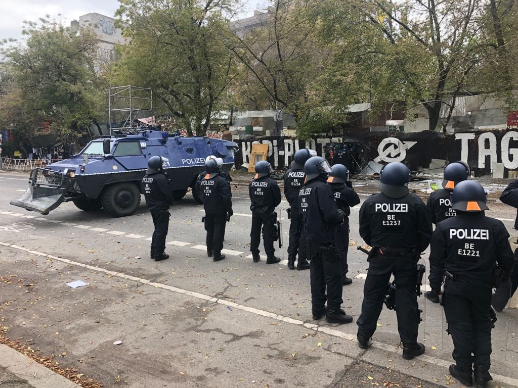 Das Räumfahrzeug der Polizei steht für den Einsatz bereit. Im Hintergrund dringen erste Einsatzkräfte auf das "Köpi"-Gelände.