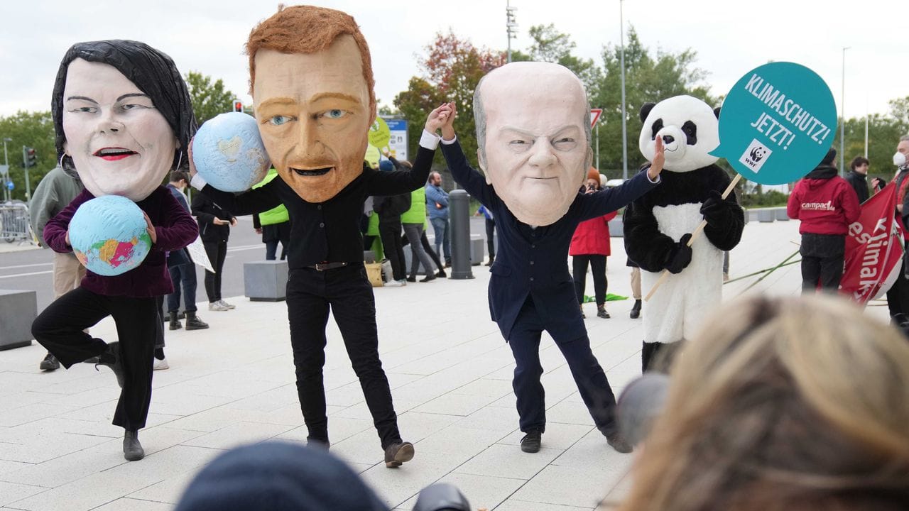 Klimaschutzaktivisten protestieren mit Masken, die Annalena Baerbock, Christian Lindner und Olaf Scholz darstellen sollen.