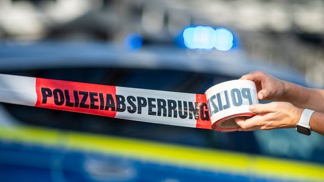 Ein Mann rollt ein Absperrband der Polizei aus