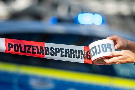 Ein Mann rollt ein Absperrband der Polizei aus