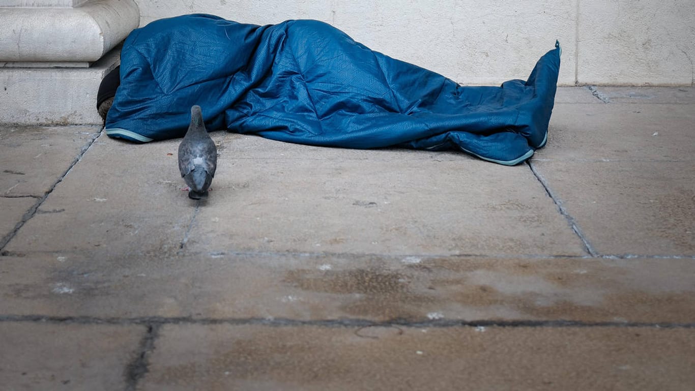 Eine obdachlos Person liegt in einem Schlafsack (Archivbild): In Köln wurde eine wohnungslose Frau im Schlaf von einem Unbekannten angegriffen.