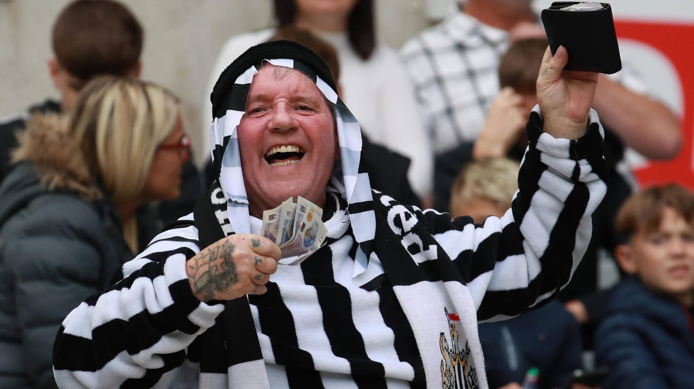 Ein verkleideter Fan von Newcastle United wedelt mit Geld auf der Tribüne.