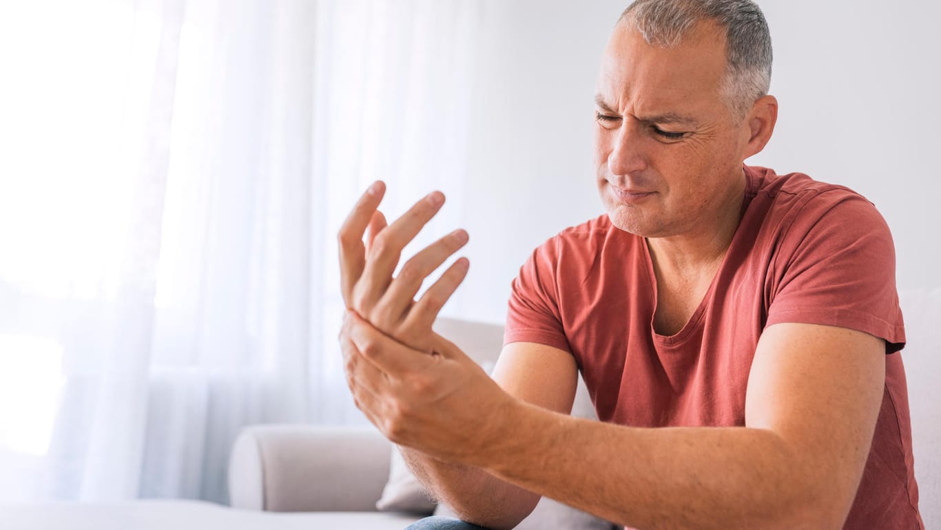 Ein Mann greift sich an die schmerzende Hand: Arthrose tritt meist einseitig auf.