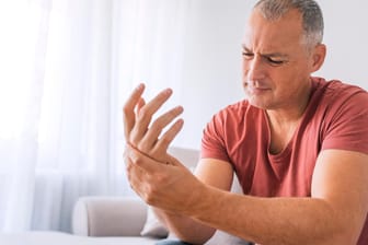Ein Mann greift sich an die schmerzende Hand: Arthrose tritt meist einseitig auf.