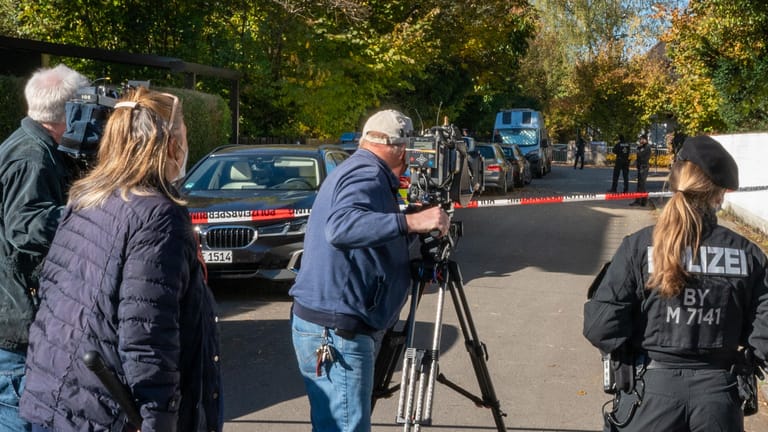 Journalisten und eine Polizistin stehen hinter einer Absperrung der Straße, in der sich der Tatort im Münchner Stadtbezirk Bogenhausen befindet: Hier ist eine 14-Jährige tot aufgefunden worden.