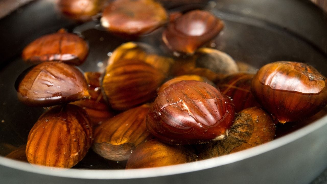 Kreuzförmig eingeritzte Maronen werden in einer Schale mit Wasser eingeweicht.