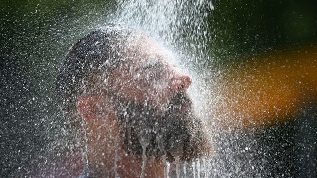 Ein Mann kühlt sich im Freibad unter einer Dusche ab.