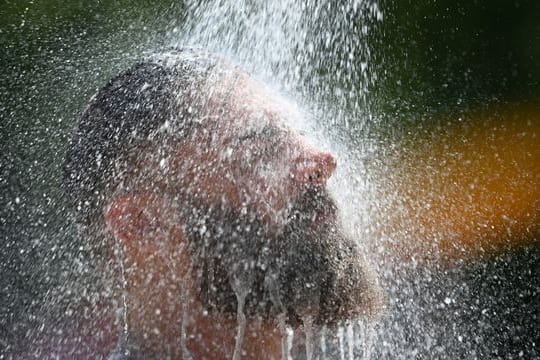 Ein Mann kühlt sich im Freibad unter einer Dusche ab.