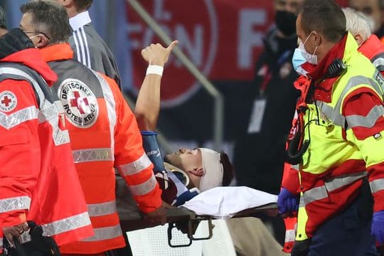 Der Nürnberger Tom Krauß (M) wird verletzt aus dem Stadion getragen, zeigt aber mit dem Daumen nach oben.