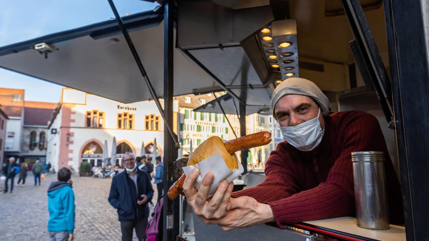Ein Wurstverkäufer steht in einem Imbisswagen auf dem Münsterplatz: Freiburg ist für die "Lange Rote" im Brötchen bekannt.