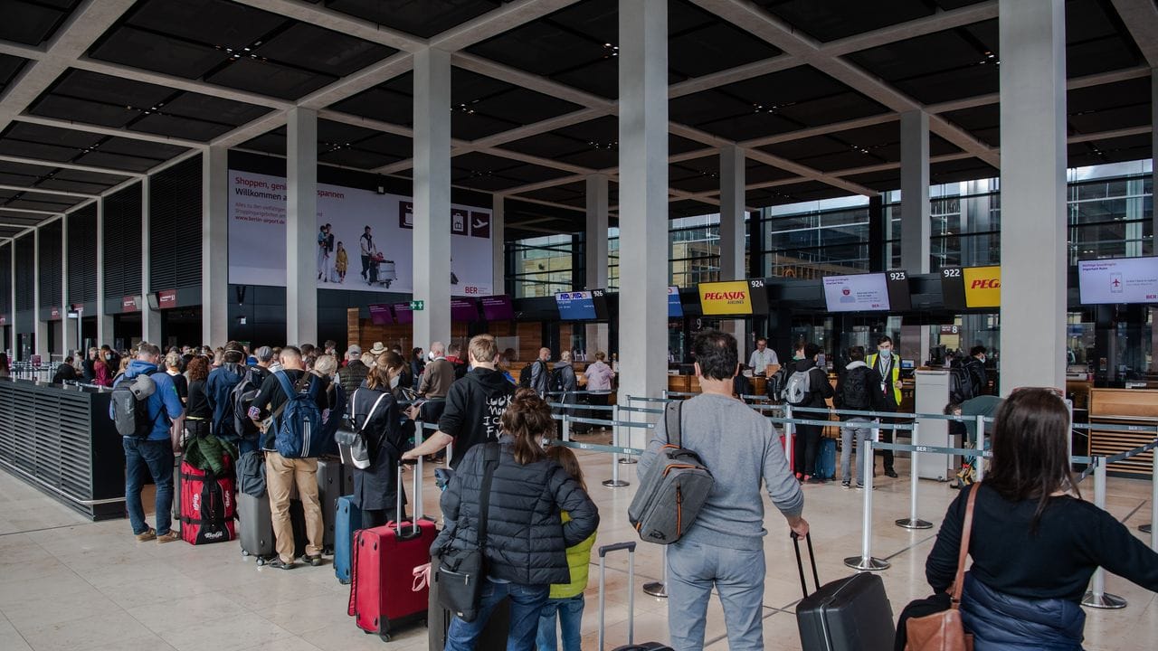 Reisende stehen am Flughafen BER vor einem Check-in-Schalter.