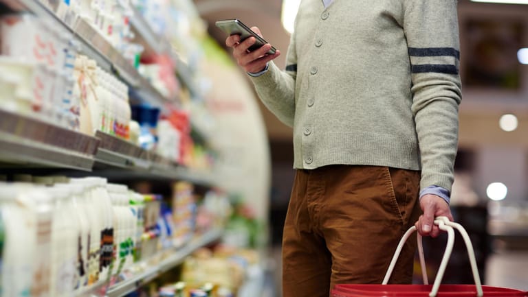 Ein Mann im Supermarkt schaut auf sein Smartphone: Worauf gilt es bei einer Schilddrüsenunterfunktion in puncto Ernährung zu achten?