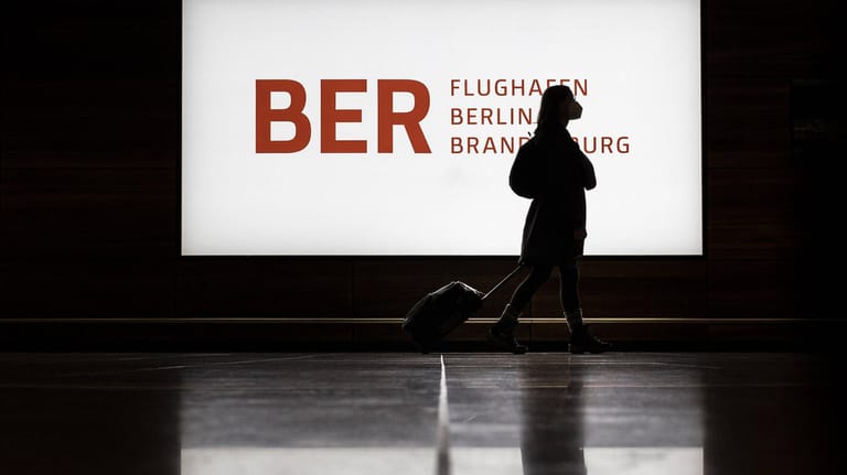 Eine Person vor dem Logo des Flughafen Willy-Brandt: Der BER braucht bis 2026 etwa 2,4 Milliarden Euro.