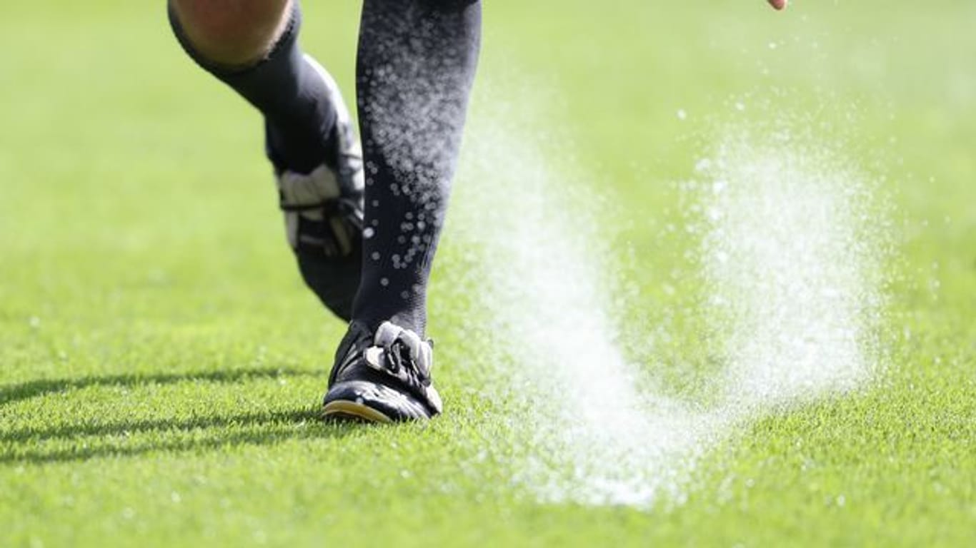 Ein Bundesliga-Schiedsrichter sprüht Freistoßspray auf den Rasen.