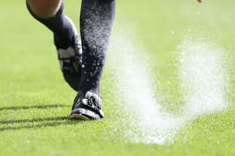 Ein Bundesliga-Schiedsrichter sprüht Freistoßspray auf den Rasen.