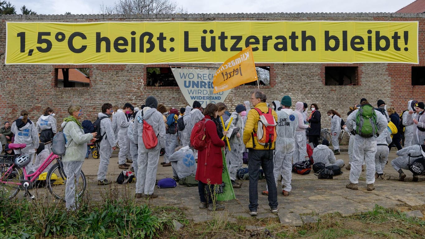 Teilnehmer stehen bei einer Demonstration vor einem der letzten Häuser von Lützerath: Ein Banner ist befestigt mit der Aufschrift "1,5 Grad Celsius heißt: Lützerath bleibt".