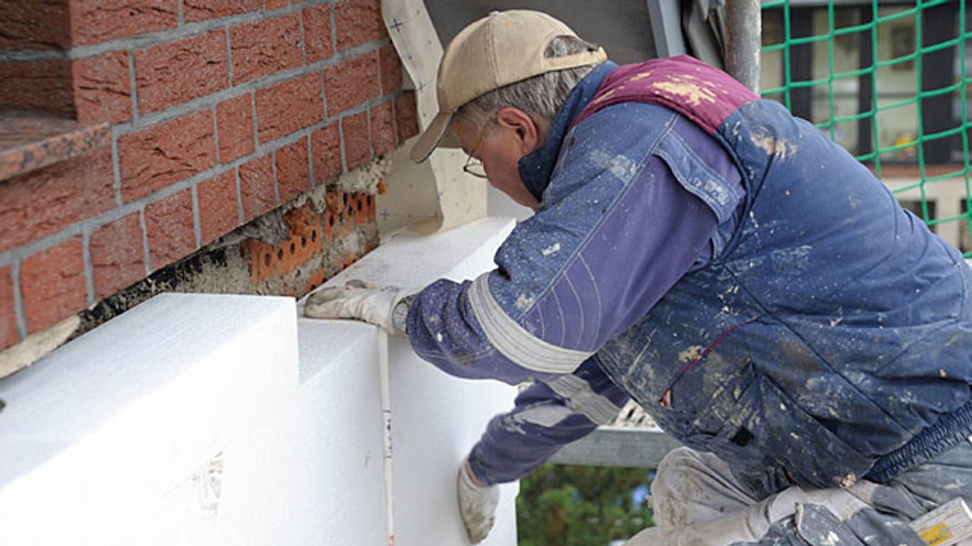 Ein Maler klebt eine 160 Millimeter dicke Styropor-Fassadendämmplatten an ein Haus