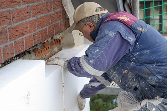 Ein Maler klebt eine 160 Millimeter dicke Styropor-Fassadendämmplatten an ein Haus