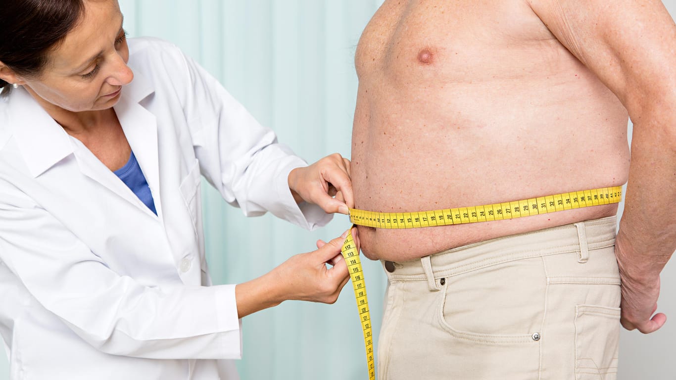 Eine Ärztin misst den Bauchumfang eines übergewichtigen älteren Mannes.