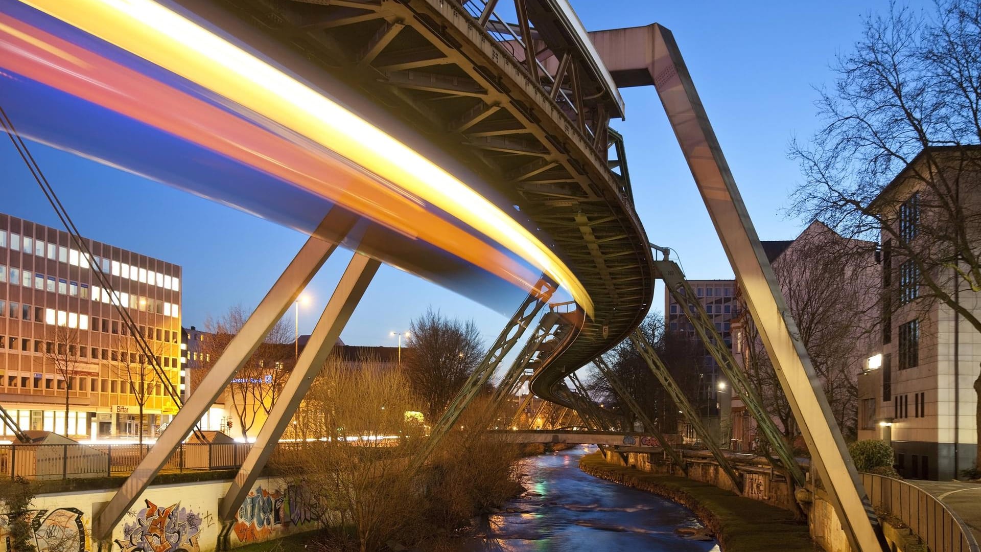 Lichtspur einer fahrenden Schwebebahn über der Wupper.