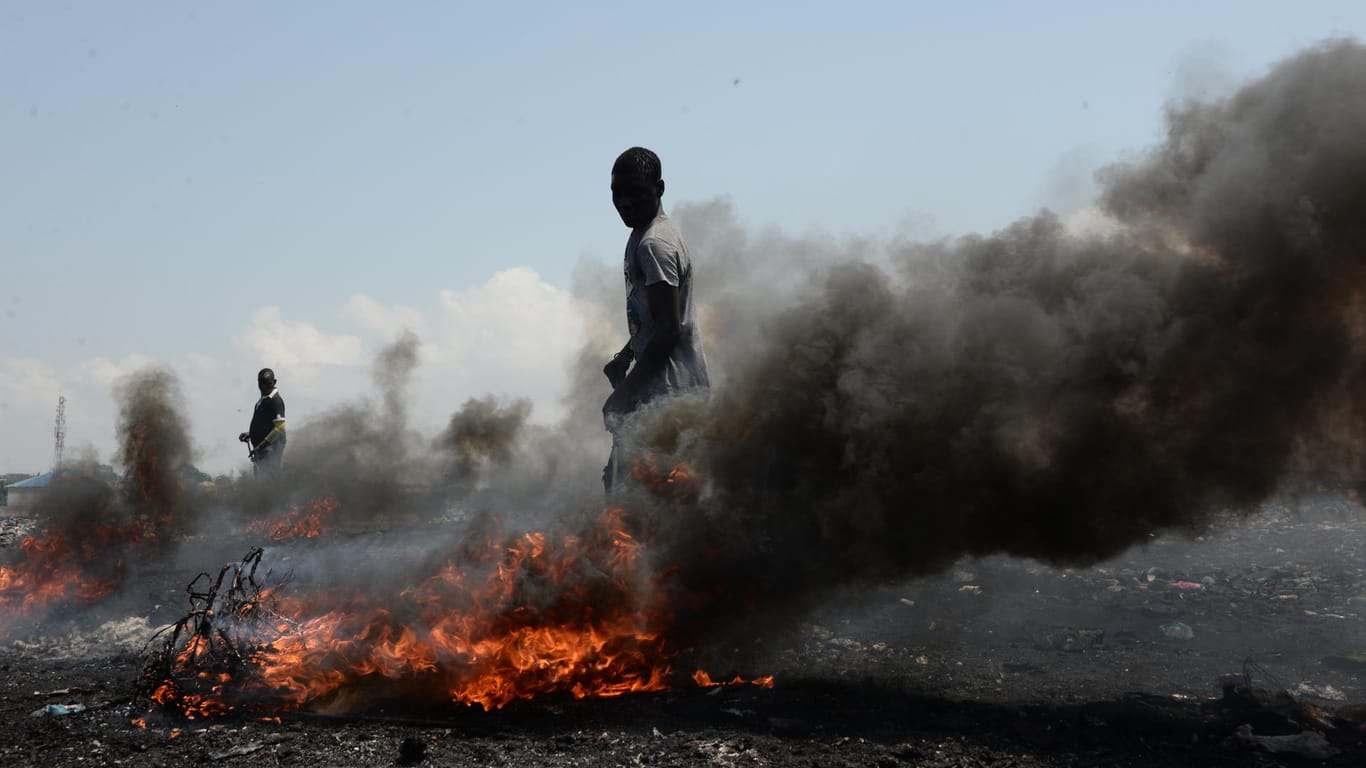 Männer verbrennen auf dem Schrottplatz Agbogbloshie Kabel und andere Teile alter Elektrogeräte, um die rohen Metalle zu gewinnen und diese weiterzuverkaufen.